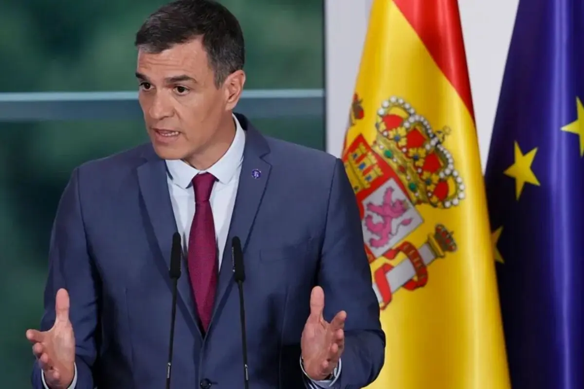Hombre con traje azul y corbata roja hablando en un atril con las banderas de España y de la Unión Europea de fondo