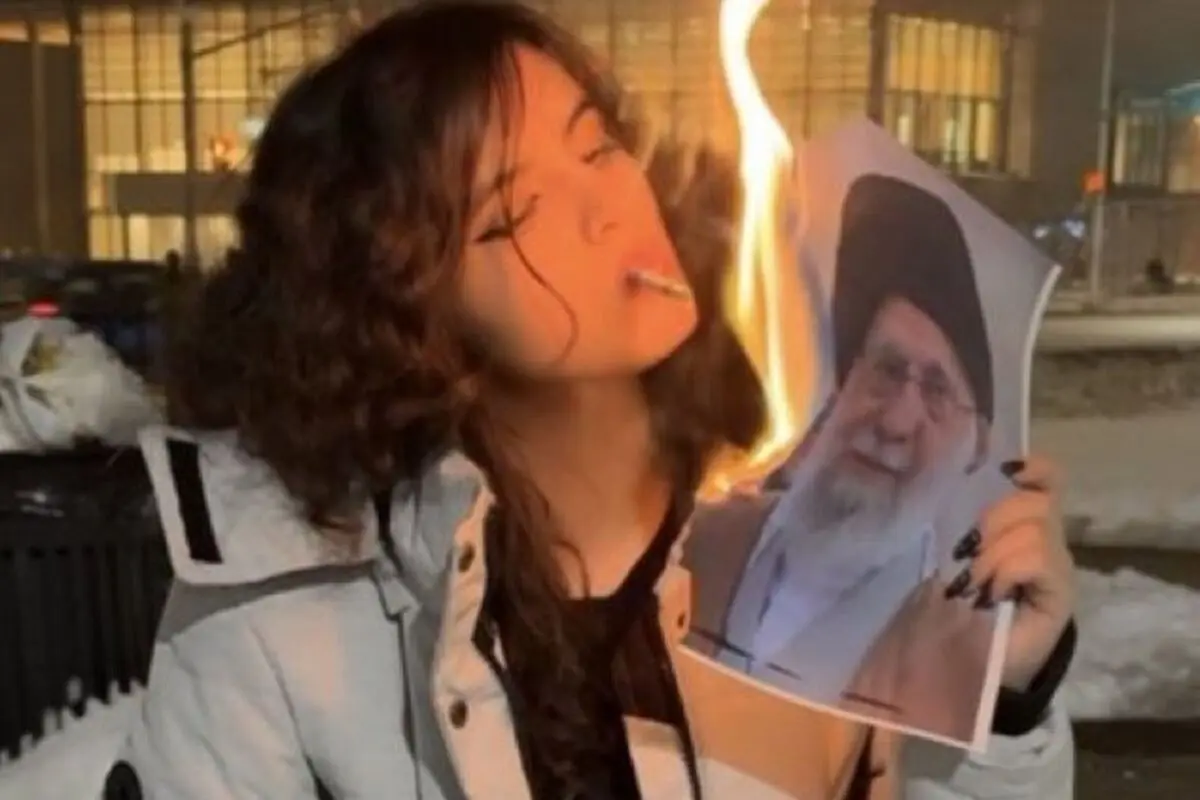 Dona jove a l’aire lliure sostenint i cremant la fotografia d’un home gran amb barba i turbant mentre fuma una cigarreta