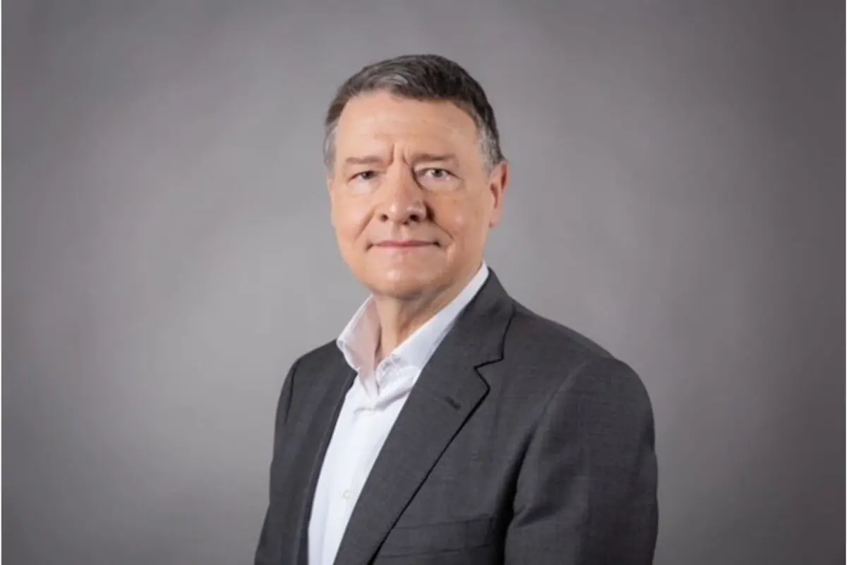 Retrato de un hombre de mediana edad con traje gris y camisa blanca posando sobre un fondo gris liso