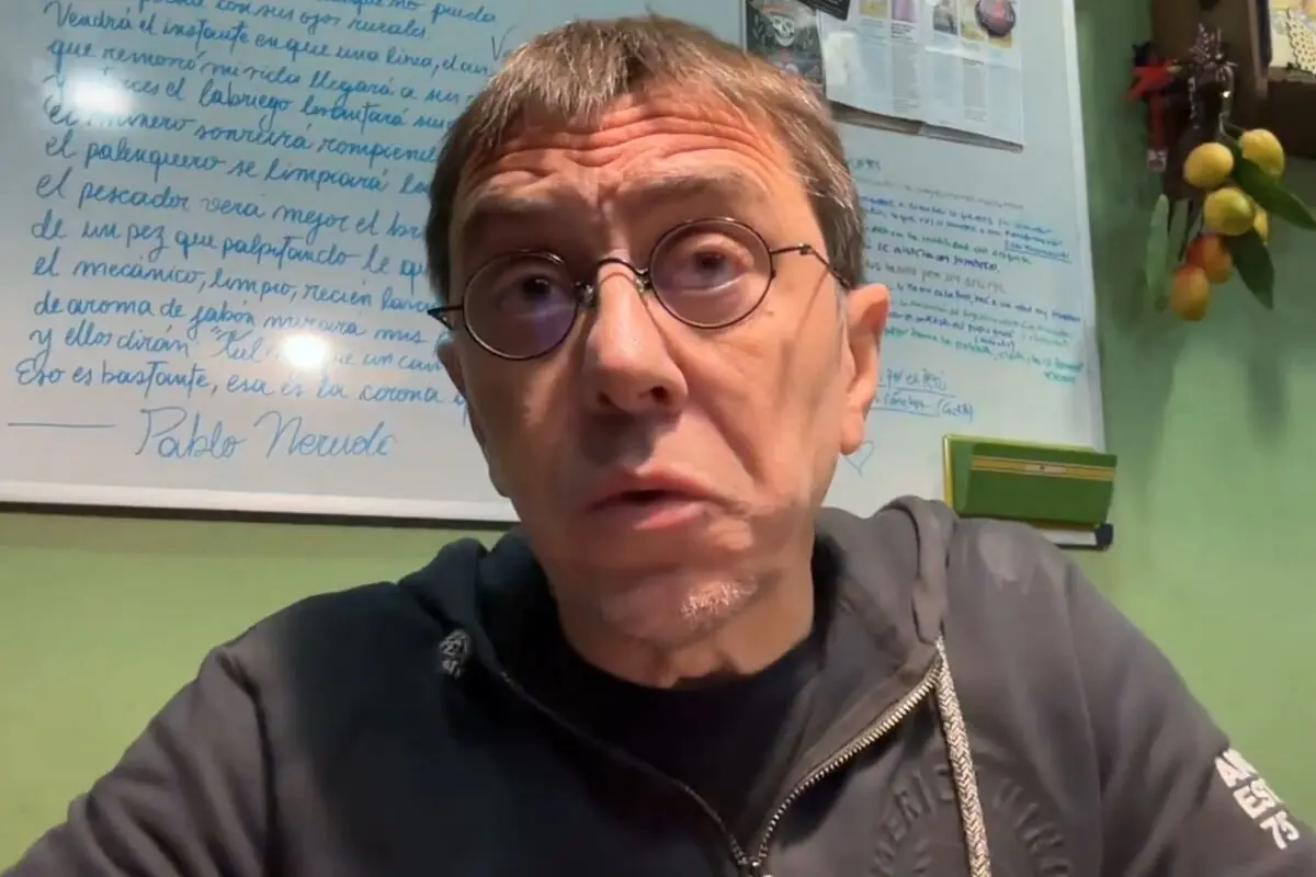 Juan Carlos Monedero amb ulleres rodones i dessuadora fosca mirant a la càmera assegut davant d’una pissarra blanca amb text escrit en blau.