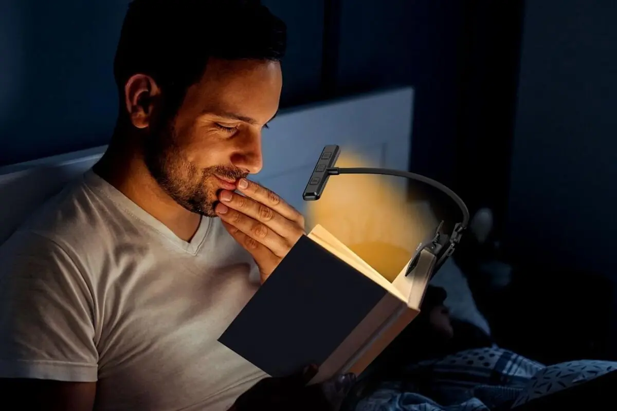 Hombre leyendo un libro en la cama por la noche iluminado por una lámpara de lectura con pinza