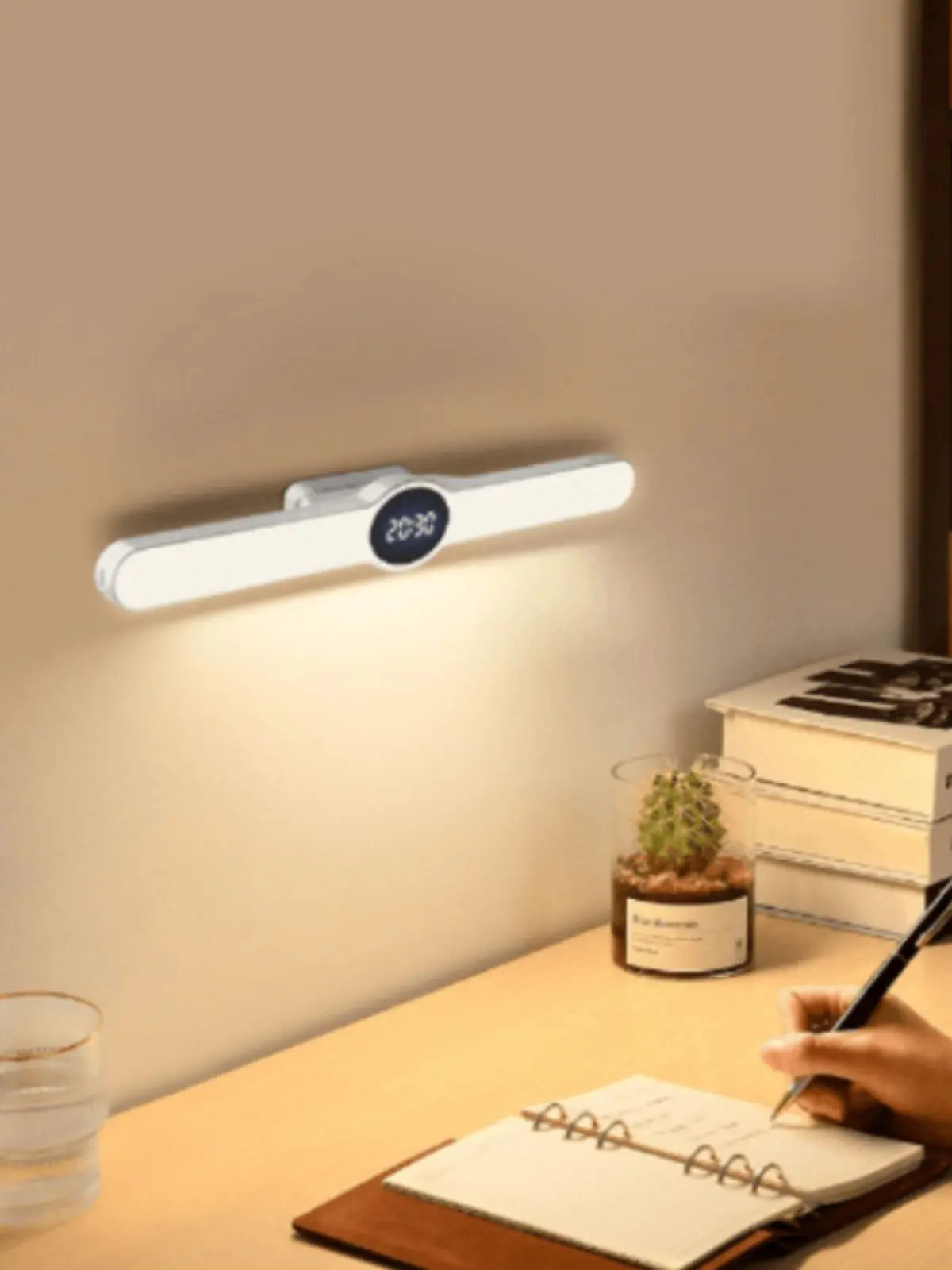 Lámpara LED de pared con reloj digital iluminando de ALDI sobre un escritorio de estudio con cuaderno cactus y libros. Lámpara LED de pared con reloj digital iluminando de ALDI sobre un escritorio de estudio con cuaderno cactus y libros.