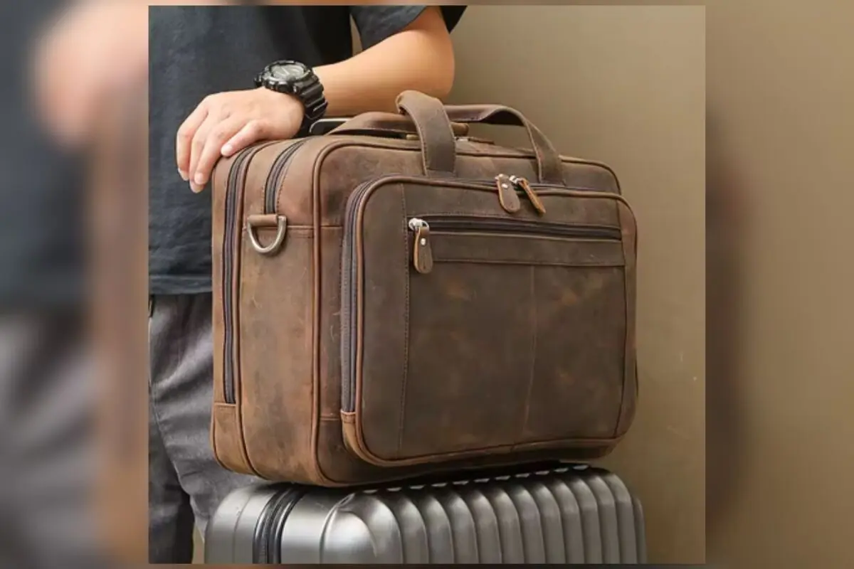 Hombre apoyando la mano sobre un maletín de cuero marrón colocado encima de una maleta rígida plateada Hombre apoyando la mano sobre un maletín de cuero marrón colocado encima de una maleta rígida plateada