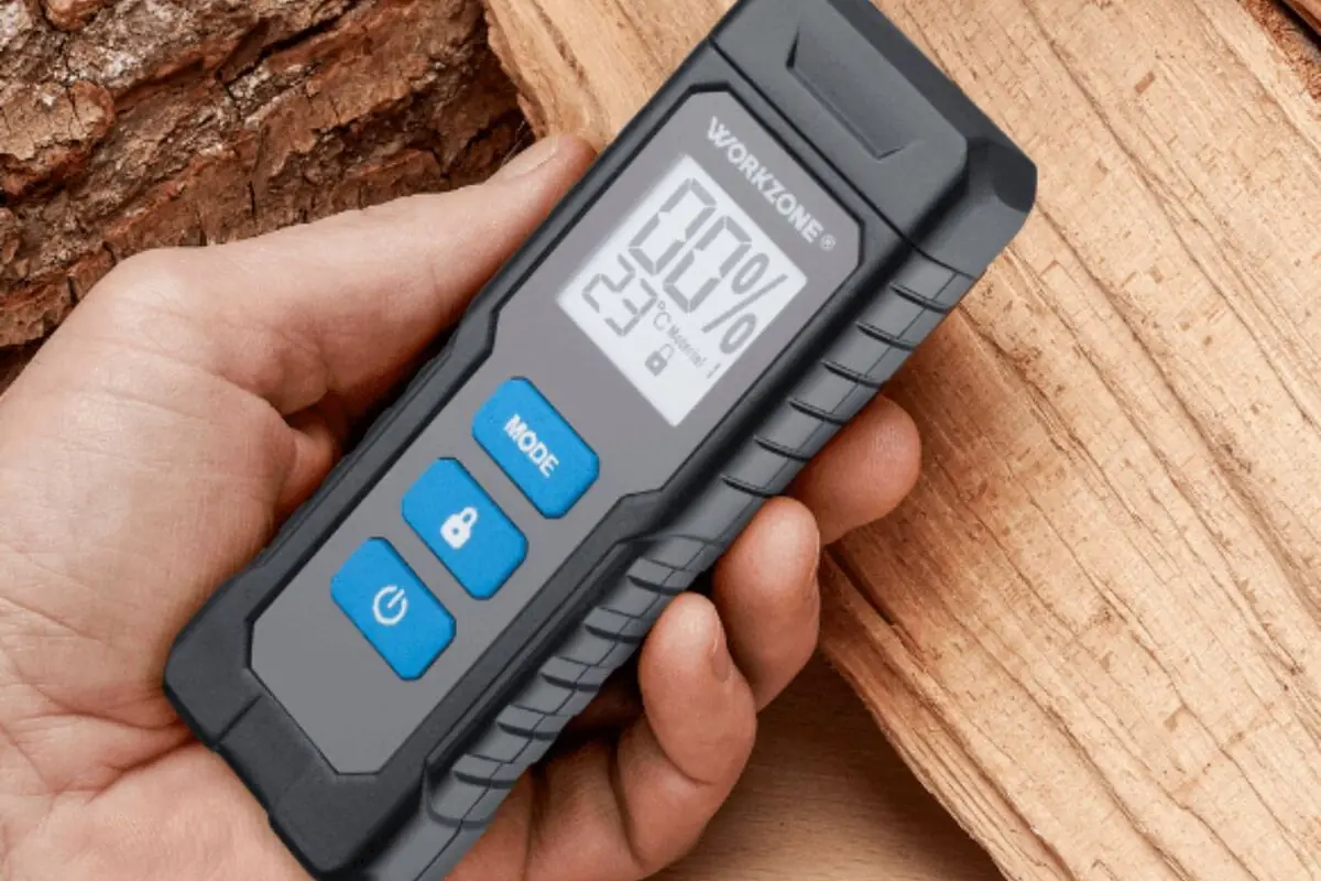Mano sosteniendo un medidor digital de humedad de la marca Workzone de Aldi sobre un trozo de madera.