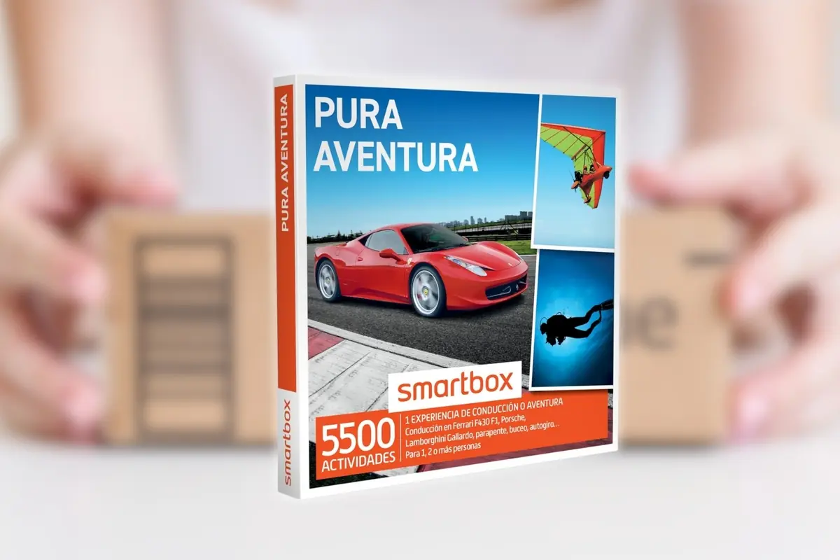 Montaje con caja de regalo Smartbox Pura Aventura con imágenes de coche deportivo rojo, vuelo en parapente y buceo y de fondo unas manos sosteniendo una caja de Amazon desenfocada