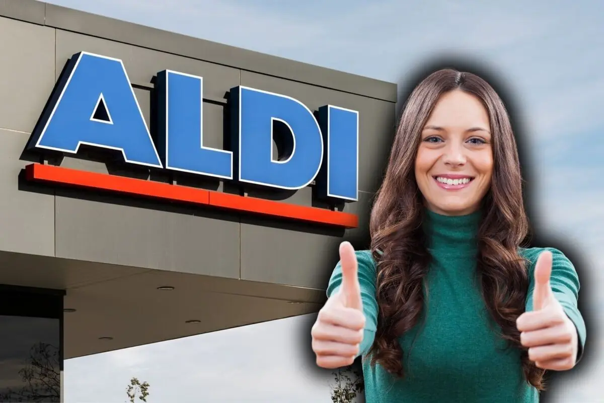 Dona jove somrient davant d’un supermercat Aldi aixecant tots dos polzes en senyal d’aprovació.
