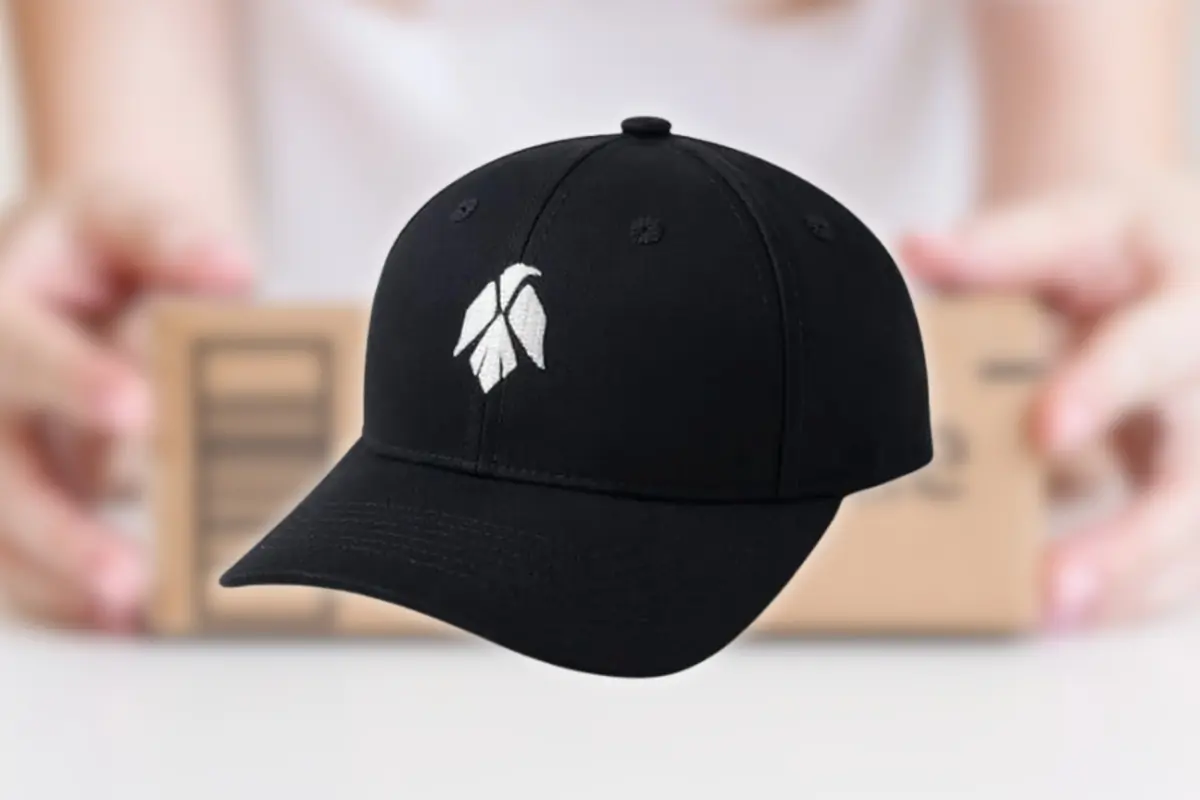 Montaje con gorra negra con logo blanco estilizado sobre fondo desenfocado de manos sosteniendo una caja de cartón