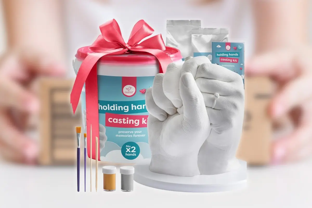 Kit de molde para manos entrelazadas con cubo decorado con lazo rojo pinceles polvos y pintura junto a una escultura blanca de dos manos sosteniéndose con un fondo desenfocado Kit de molde para manos entrelazadas con cubo decorado con lazo rojo pinceles polvos y pintura junto a una escultura blanca de dos manos sosteniéndose con un fondo desenfocado