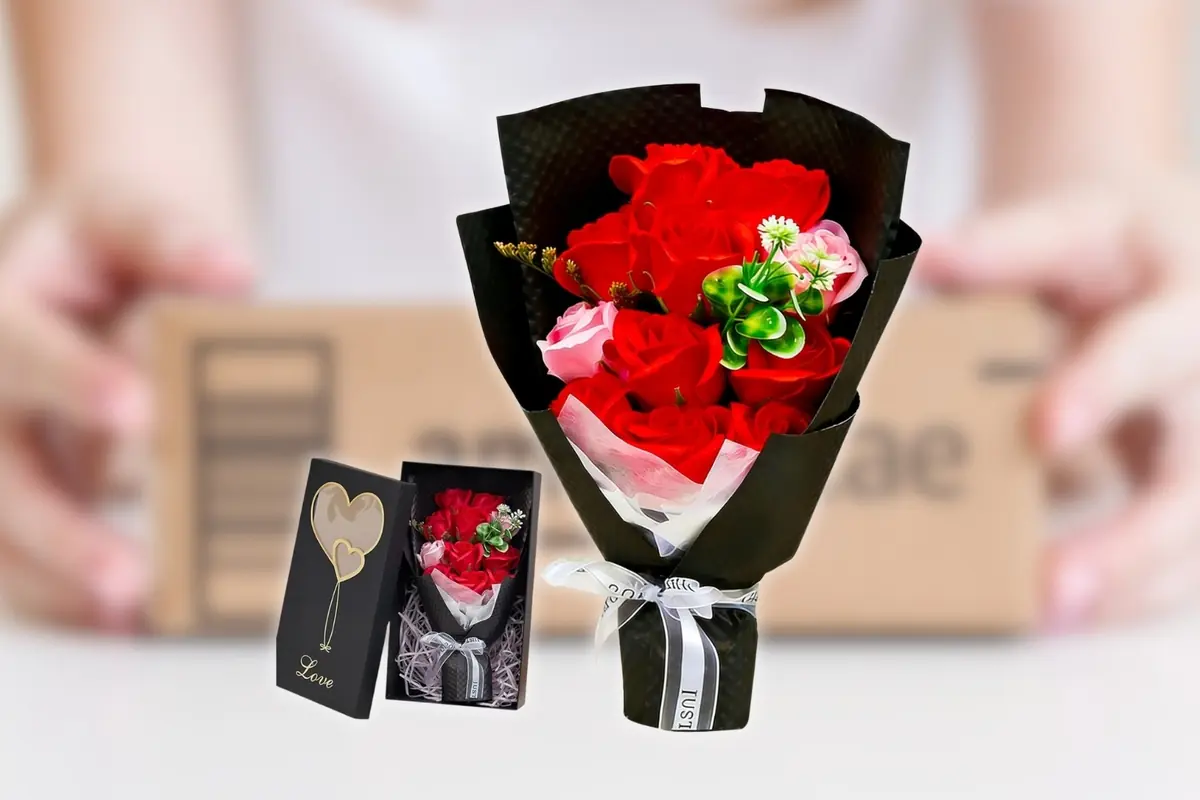 Ramo de rosas rojas y rosas con follaje verde envuelto en papel negro elegante junto a su caja de regalo negra con diseño de corazón, y de fondo una caja desenfocada
