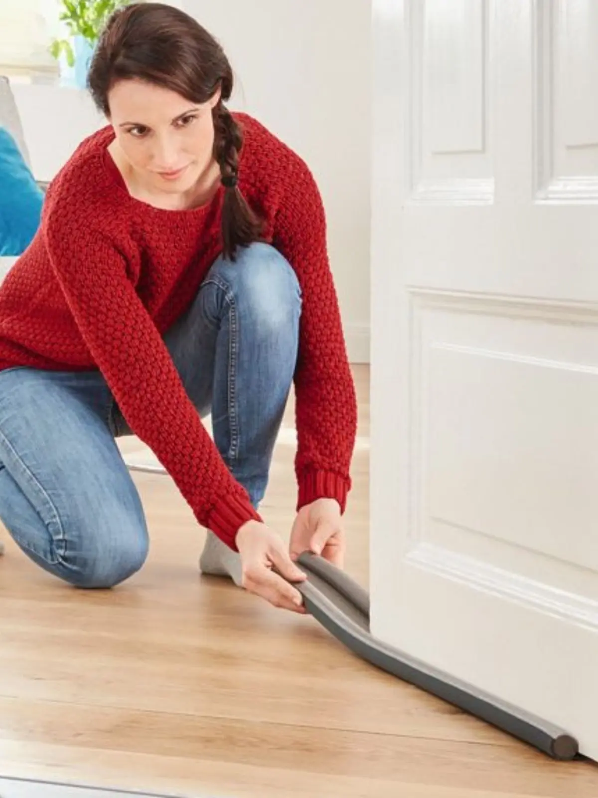 Mujer arrodillada en el suelo colocando un burlete aislante de Aldi en la parte inferior de una puerta blanca para evitar corrientes de aire.