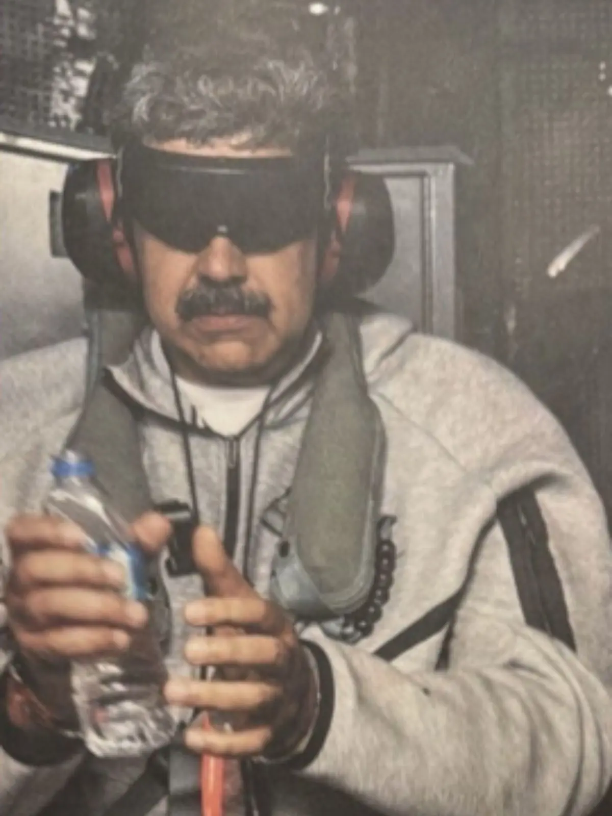 Nicolás Maduro amb antifaç negre i orelleres vermelles assegut en un seient entapissat mentre sosté una ampolla d’aigua amb totes dues mans.