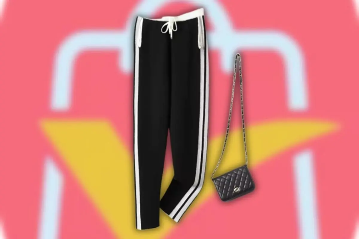 Pantalón deportivo negro con franjas blancas a los lados junto a un bolso pequeño negro acolchado con cadena sobre fondo rosa con figura de bolsa de compras