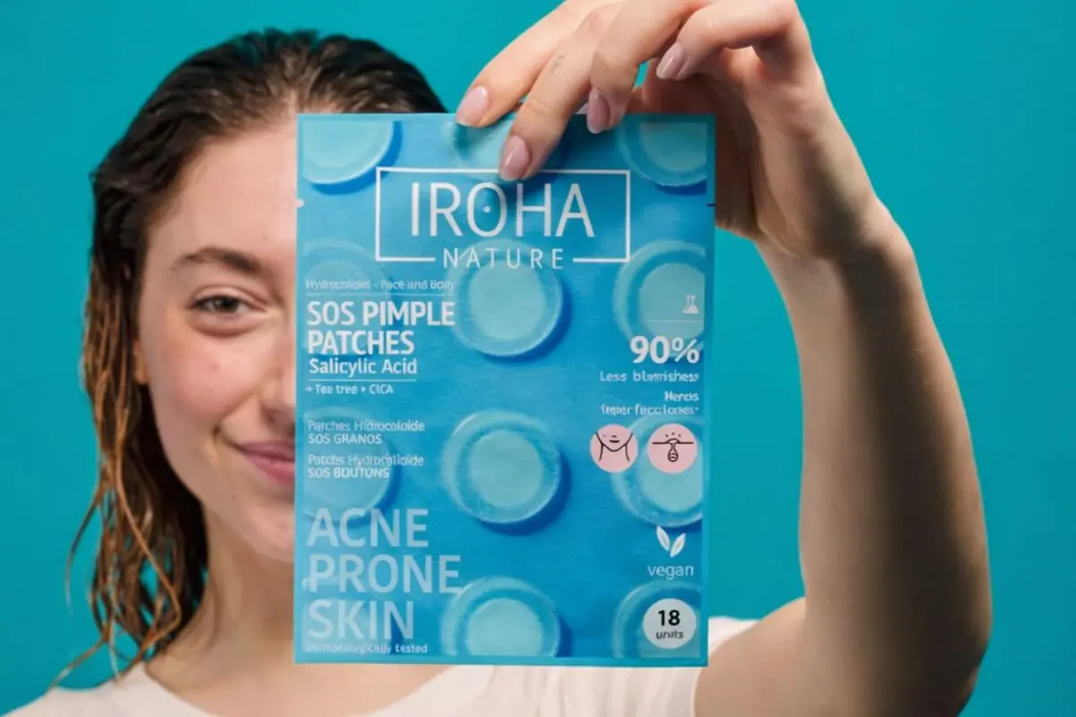 Mujer joven con el cabello húmedo sosteniendo frente a su rostro un paquete azul de parches para granos Iroha Nature para piel con acné