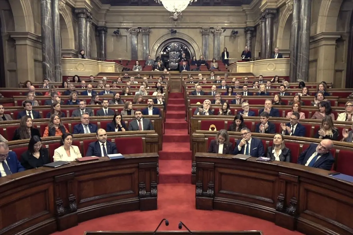 Pleno parlamentario con numerosos diputados sentados en escaños rojos dentro de un gran salón institucional con columnas y lámpara de araña