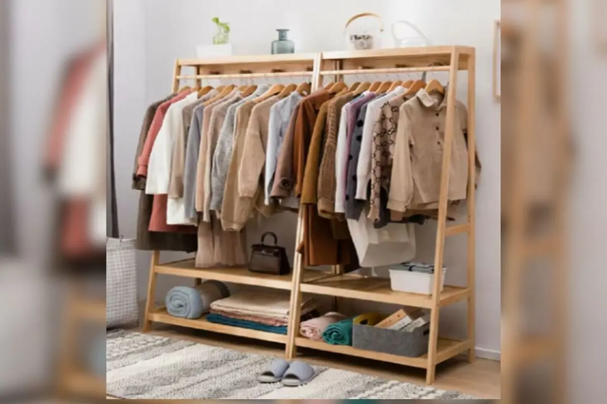 Perchero de madera con ropa colgada en tonos neutros y estantes inferiores con mantas cajas y accesorios de almacenamiento