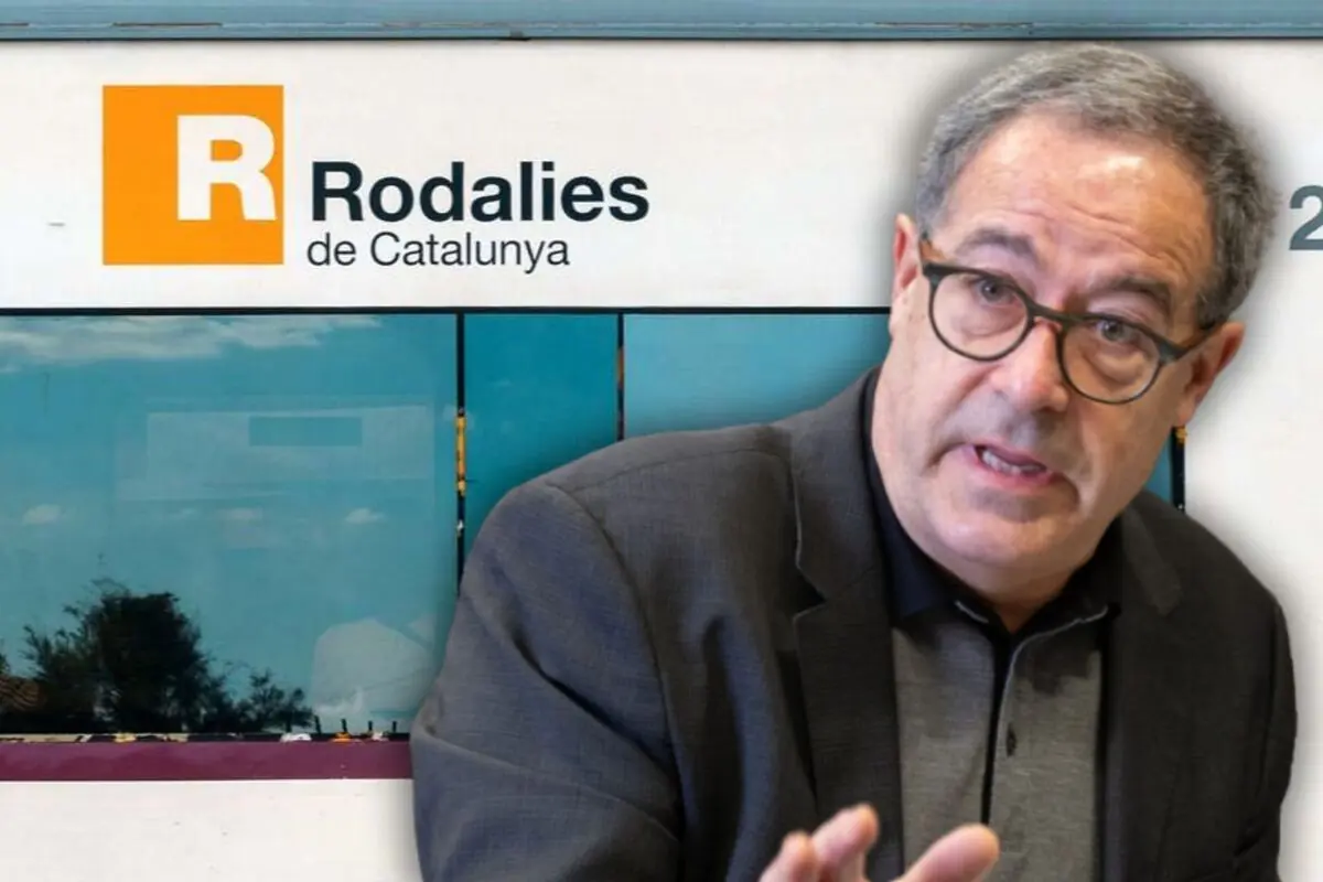 Hombre con gafas y chaqueta oscura hablando en primer plano frente a un cartel de Rodalies de Catalunya