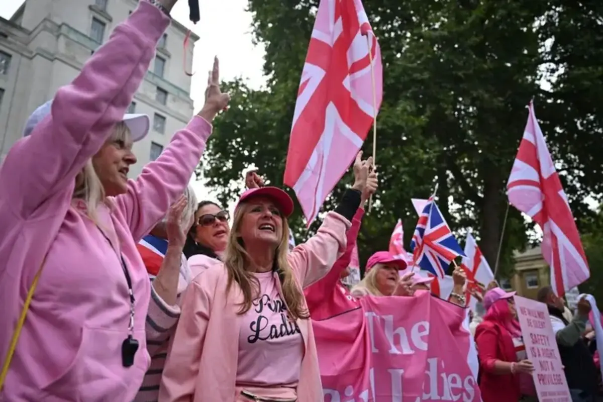 Grupo de mujeres vestidas de rosa agitando banderas del Reino Unido y pancartas durante una manifestación al aire libre