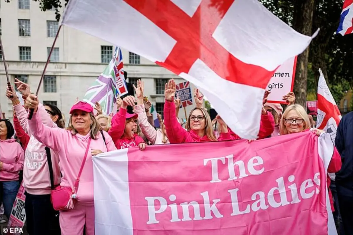 Grupo de mujeres vestidas de rosa sosteniendo una gran pancarta que dice The Pink Ladies y agitando banderas en una manifestación al aire libre Grupo de mujeres vestidas de rosa sosteniendo una gran pancarta que dice The Pink Ladies y agitando banderas en una manifestación al aire libre