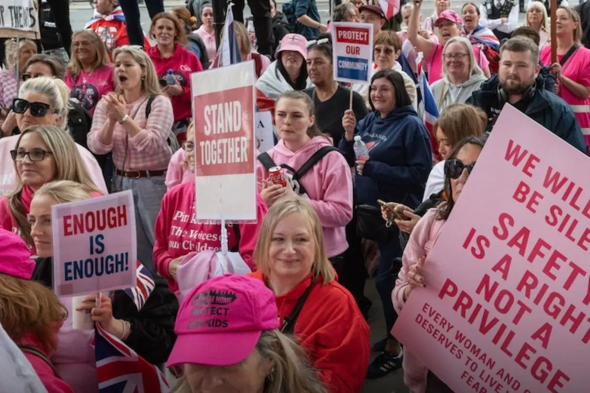 Grupo de personas, en su mayoría mujeres con ropa rosa, participando en una manifestación y sosteniendo pancartas con mensajes de protesta sobre seguridad y protección de la comunidad Grupo de personas, en su mayoría mujeres con ropa rosa, participando en una manifestación y sosteniendo pancartas con mensajes de protesta sobre seguridad y protección de la comunidad
