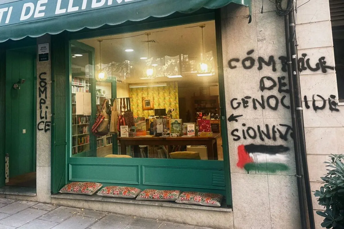 Façana d’una llibreria amb aparador verd i coixins a la vorera, coberta de pintades de protesta a les parets exteriors