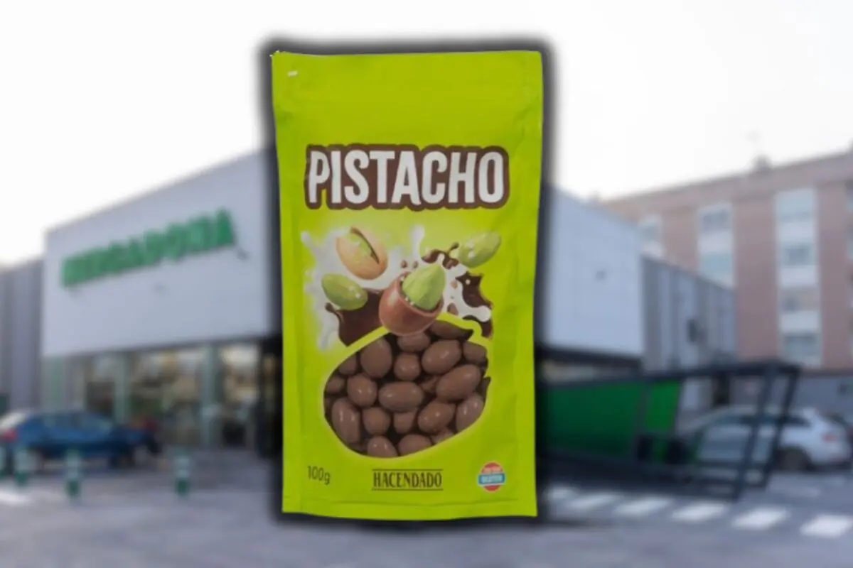 Bolsa verde de pistachos cubiertos de chocolate marca Hacendado frente a un supermercado Mercadona desenfocado