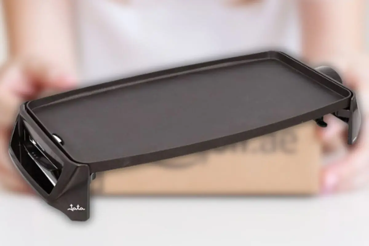 Plancha eléctrica de cocina negra rectangular sobre fondo desenfocado con una persona sosteniendo una caja detrás