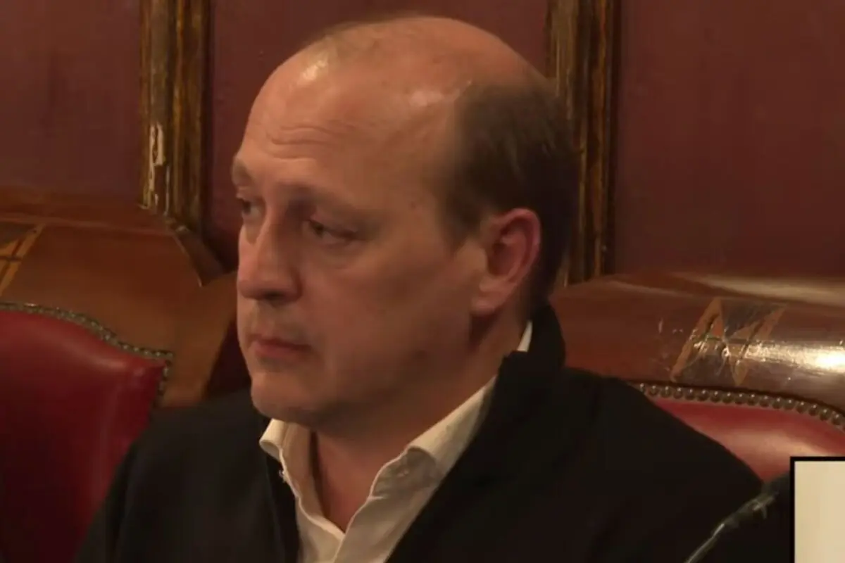 Home calb de mitjana edat amb expressió seriosa assegut en un silló de cuir vermell en una sala amb parets fosques