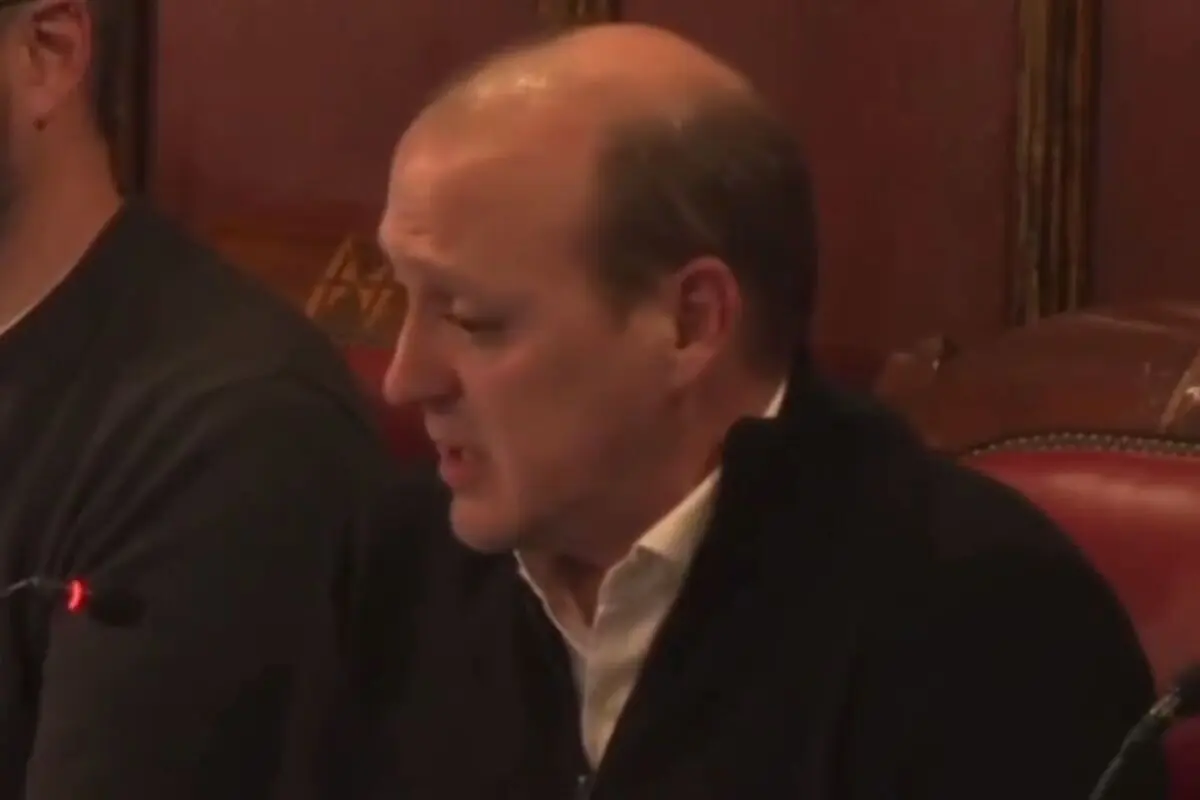 Home calb de mitjana edat parlant davant d’un micròfon en una sala amb seients de cuir vermell