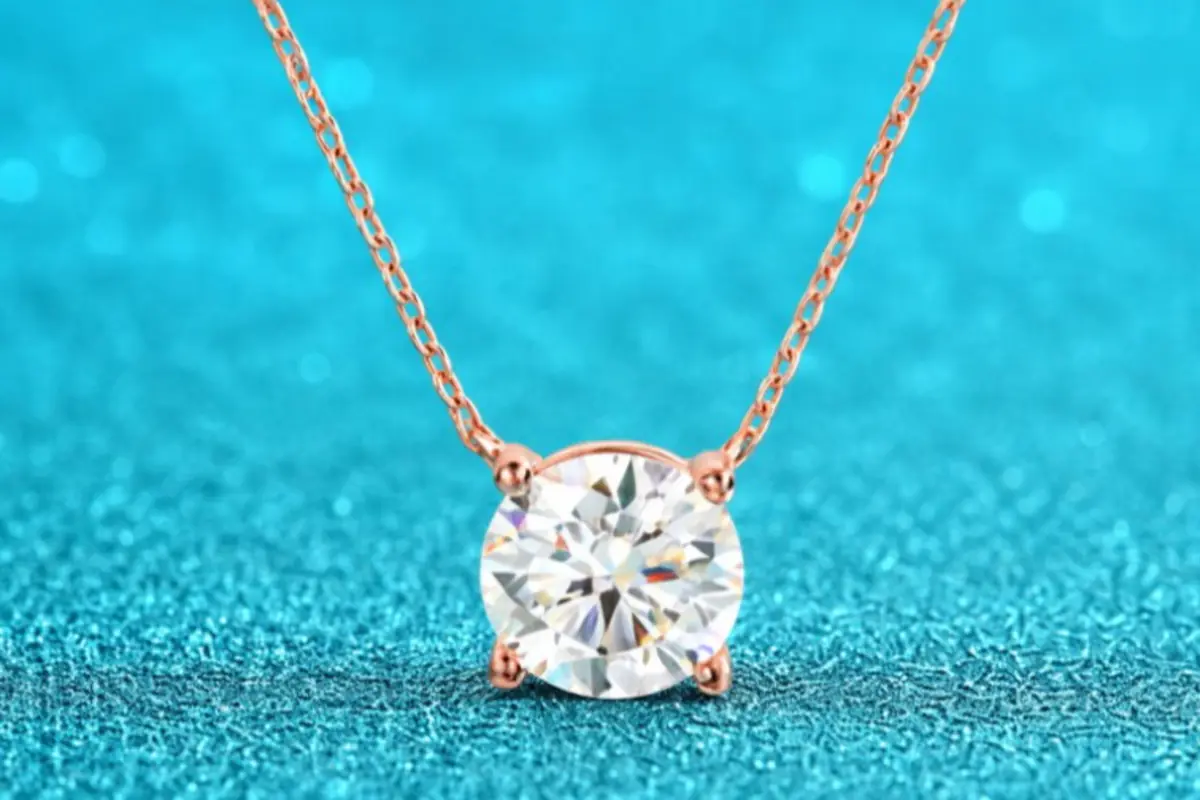 Collar de cadena fina en oro rosa con colgante de diamante redondo sobre fondo turquesa brillante