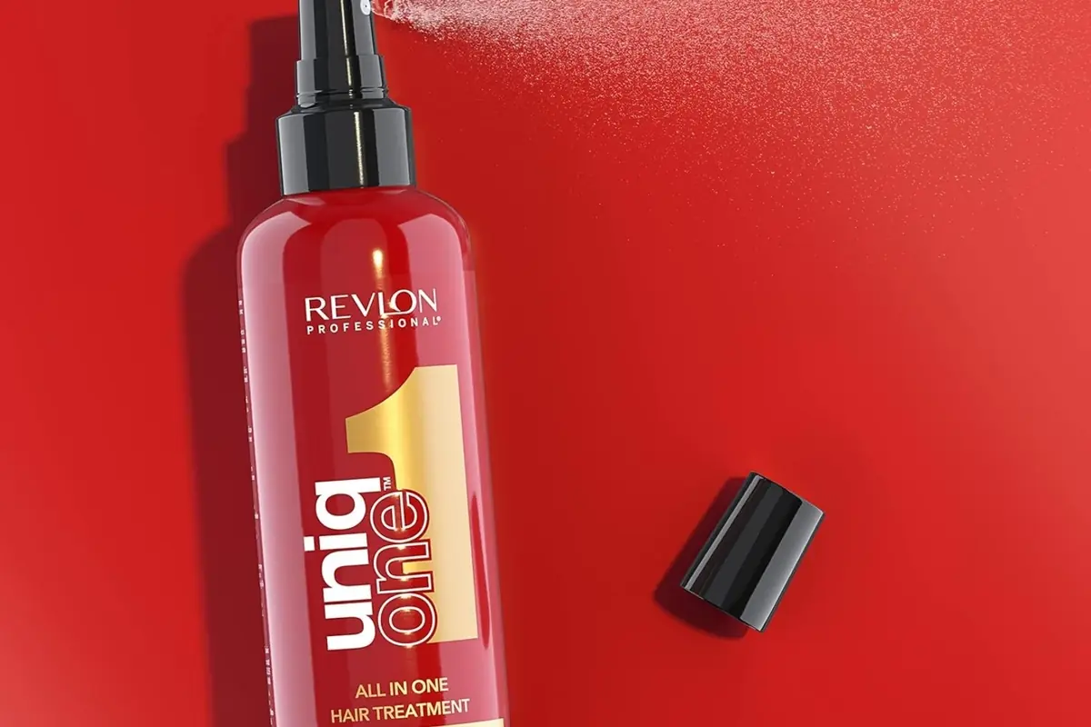 Botella roja de spray capilar Revlon Uniq One en fondo rojo con tapa negra apoyada al lado