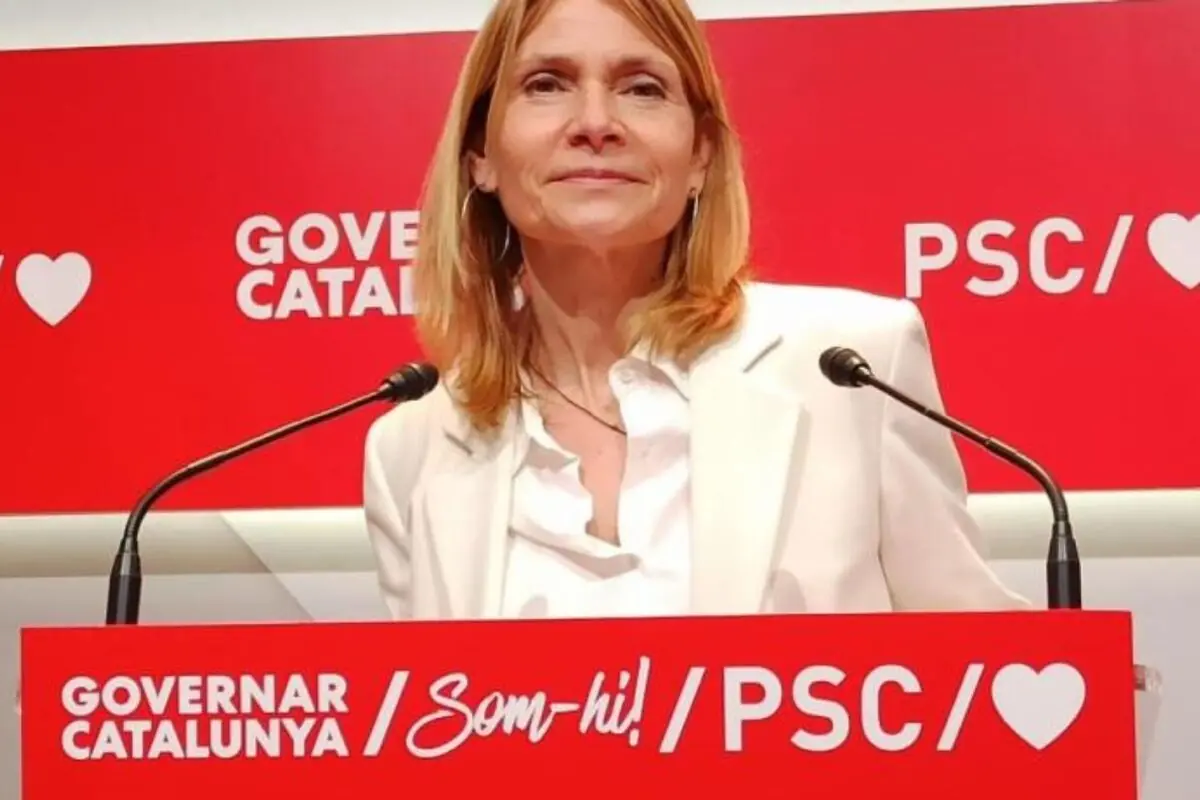 Dona amb jaqueta blanca parlant en un faristol vermell del PSC amb el lema Governar Catalunya Som-hi