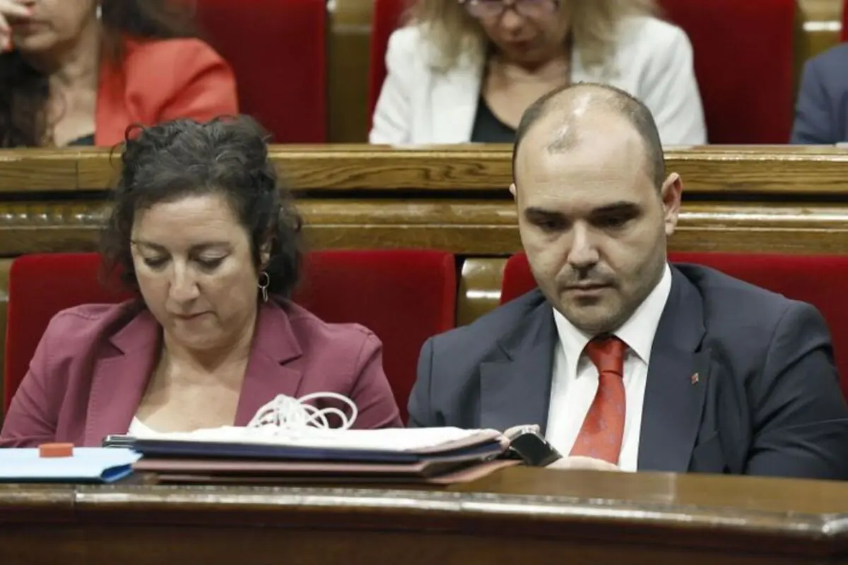 Dues persones assegudes en bancs vermells d’un parlament revisen documents i un telèfon mòbil durant una sessió