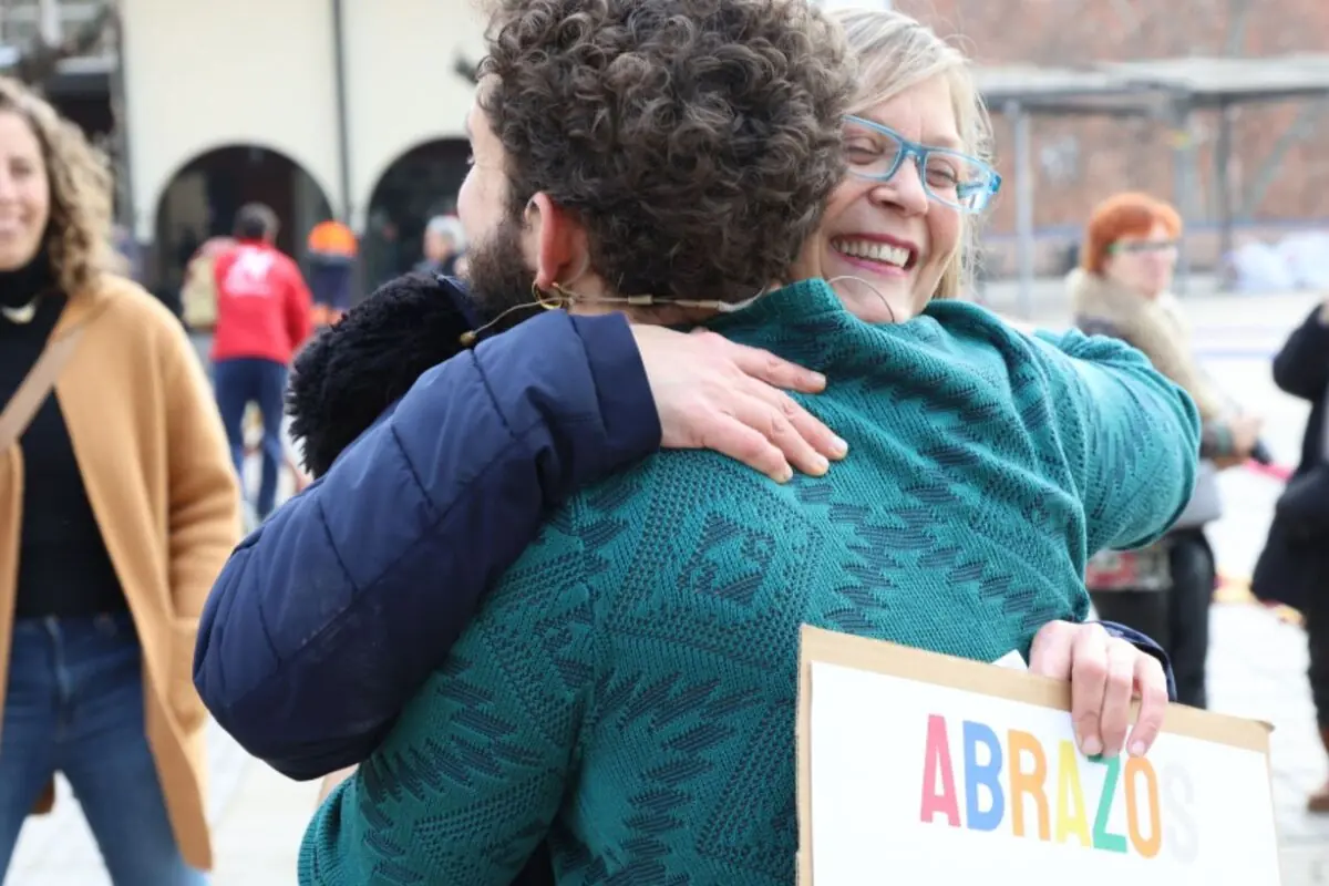 Dona somrient abraça un home al carrer mentre sosté un cartell que diu ABRAÇADES