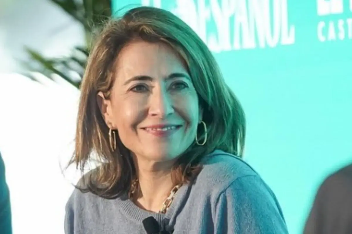 Raquel Sánchez somrient en un esdeveniment amb fons turquesa i micròfon subjectat a la roba.