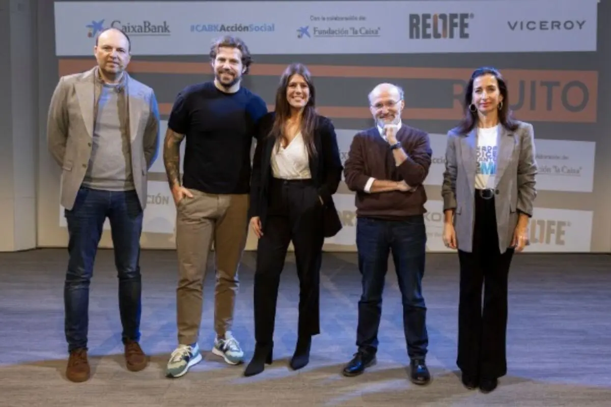 Cinc persones posen dretes en un escenari d’un esdeveniment corporatiu amb un fons on es veuen logotips de CaixaBank i d’altres marques