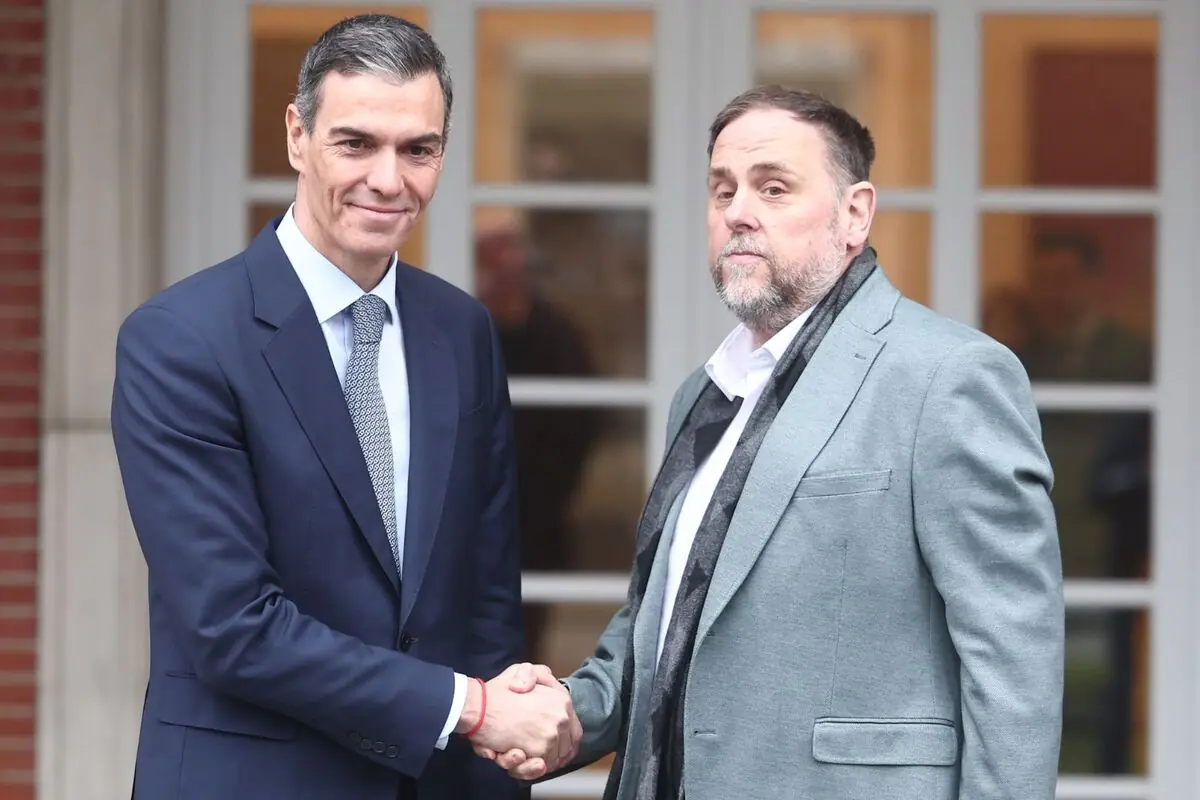 Dos homes de mitjana edat vestits amb vestit es donen la mà davant de l’entrada d’un edifici amb grans finestrals