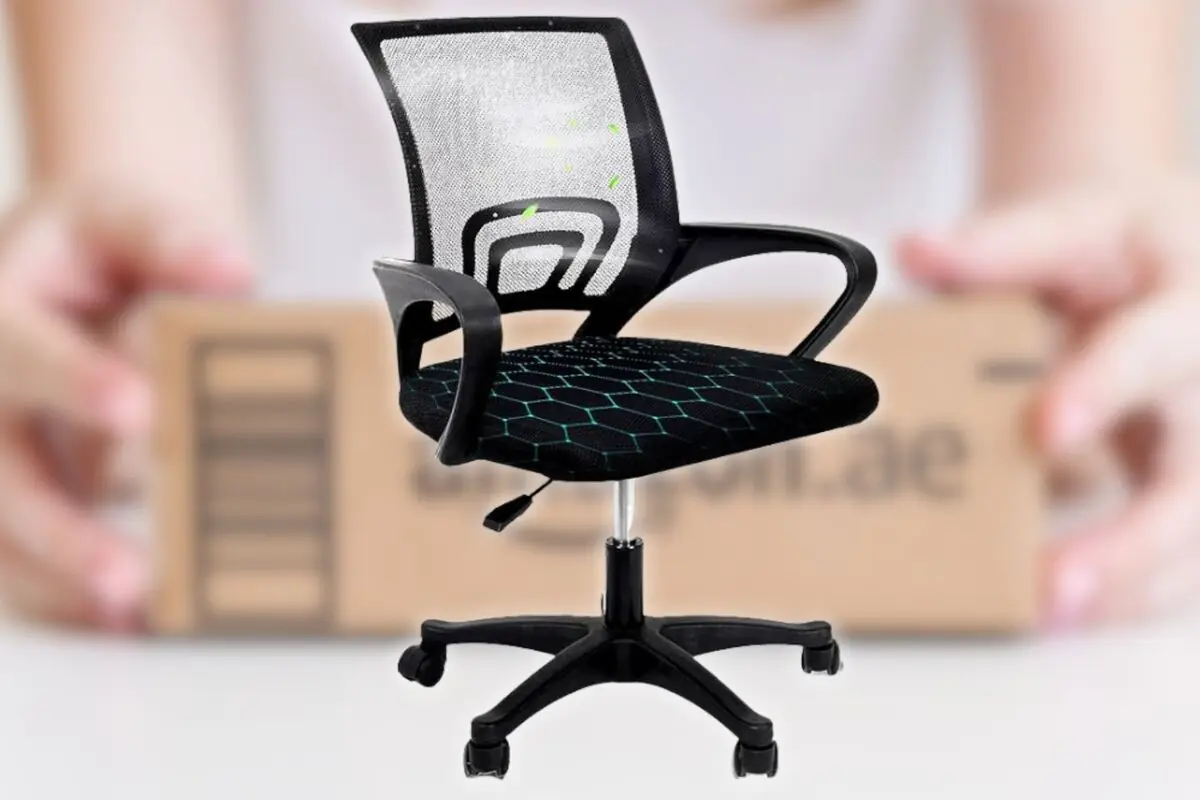 Silla de oficina negra con respaldo de malla y asiento acolchado sobre base giratoria con ruedas frente a una caja de cartón desenfocada