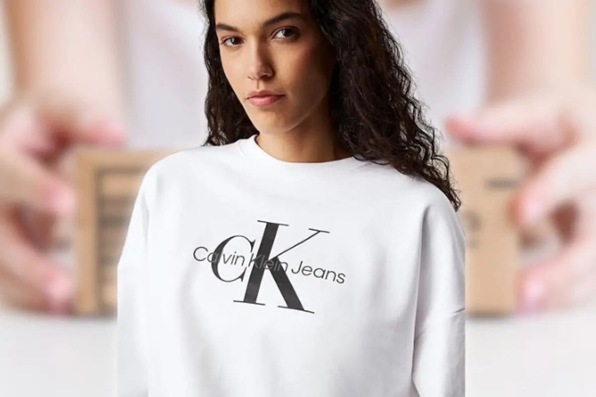 Mujer joven con sudadera blanca de Calvin Klein Jeans sobre fondo desenfocado