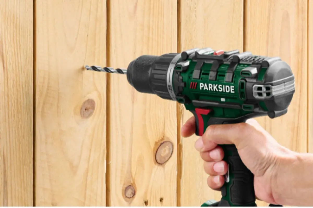 Parkside cordless electric drill drilling a wooden board held by a hand