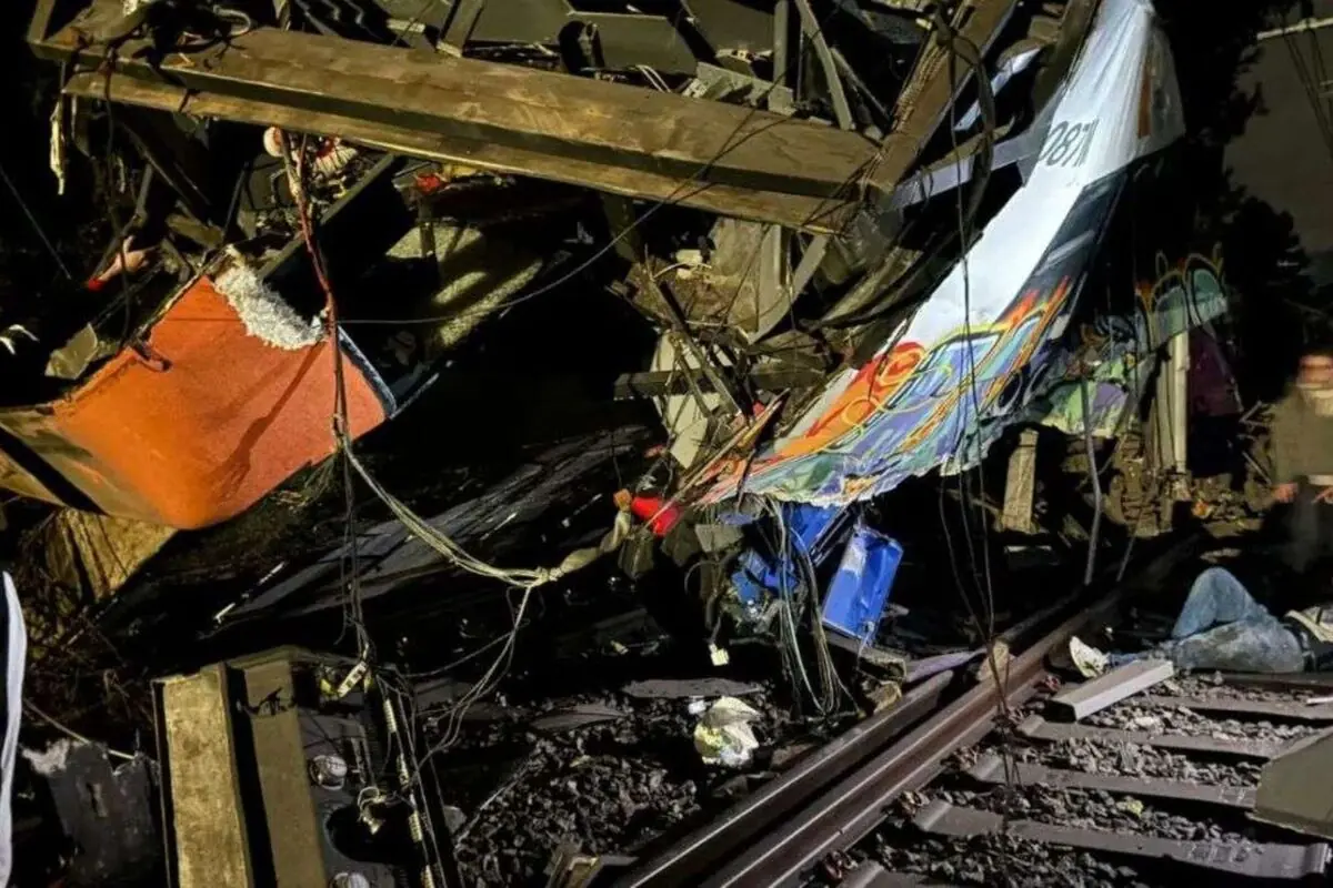 Vagón de tren gravemente destrozado sobre las vías en la noche con restos metálicos cables sueltos y una persona tendida en el suelo entre los escombros