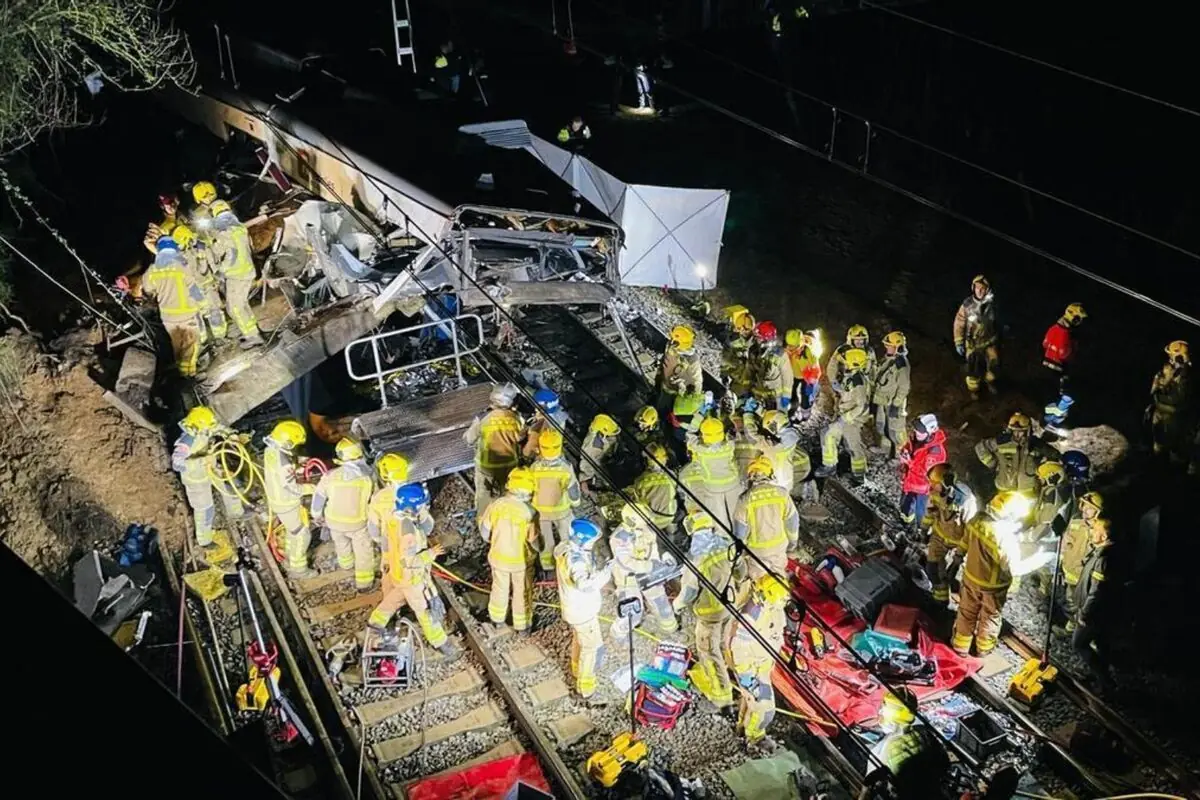 Decenas de bomberos con cascos y chalecos reflectantes trabajan de noche entre los restos de un tren descarrilado sobre las vías realizando labores de rescate y emergencia