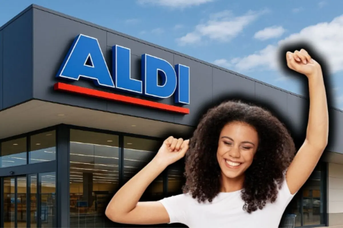 Mujer joven sonriente levantando los brazos frente a la fachada de un supermercado Aldi.