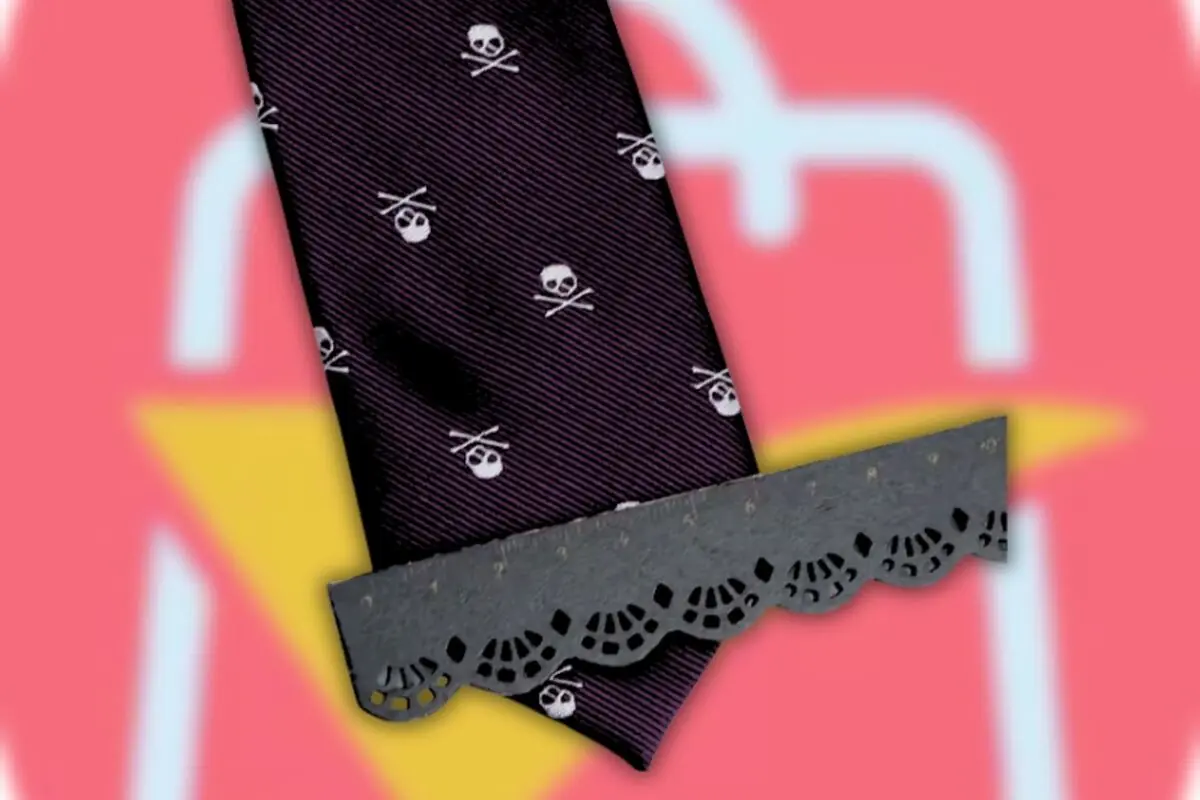Corbata negra con estampado de calaveras cruzadas parcialmente cubierta por una regla decorativa sobre un fondo rosa con forma de bolsa de compras estilizada