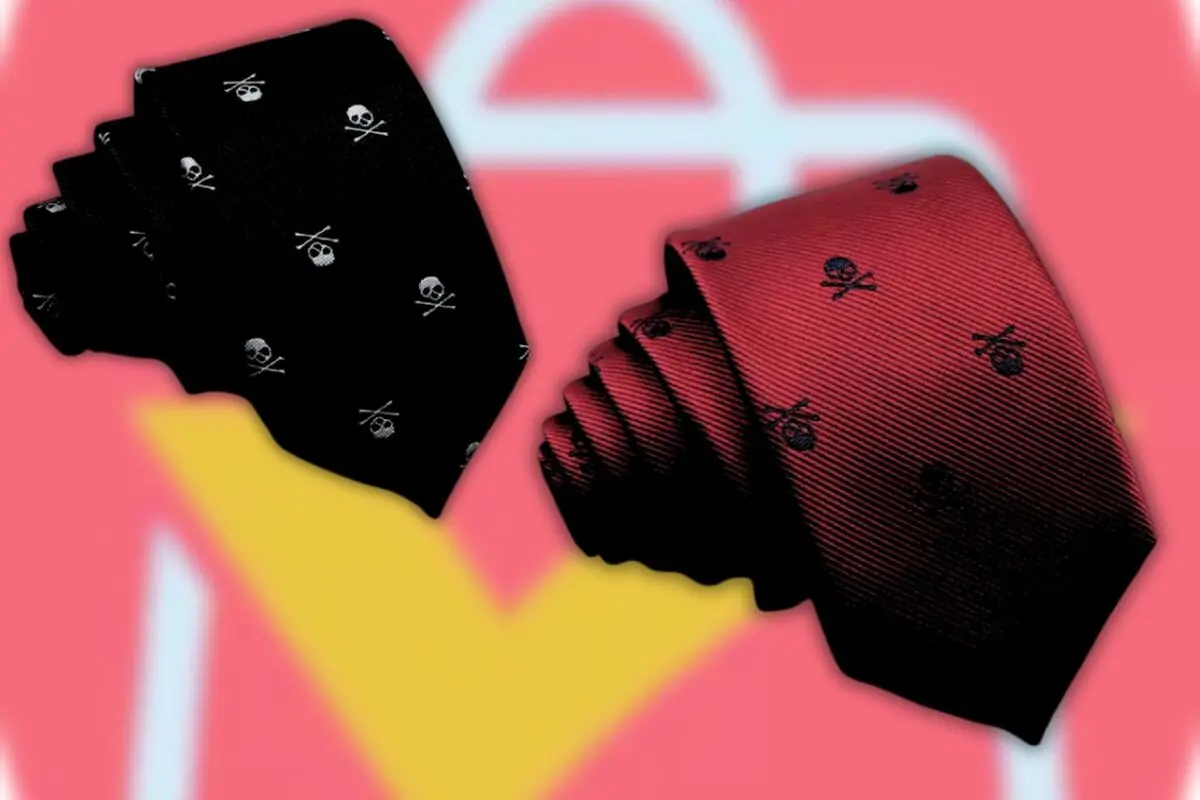 Dos corbatas elegantes una negra y otra roja con pequeños estampados de calaveras cruzadas sobre un fondo rosa difuminado