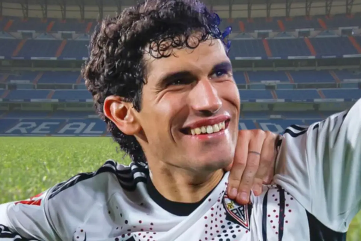 Futbolista sonriente con uniforme blanco y negro celebrando en un estadio de fútbol con gradas azules de fondo