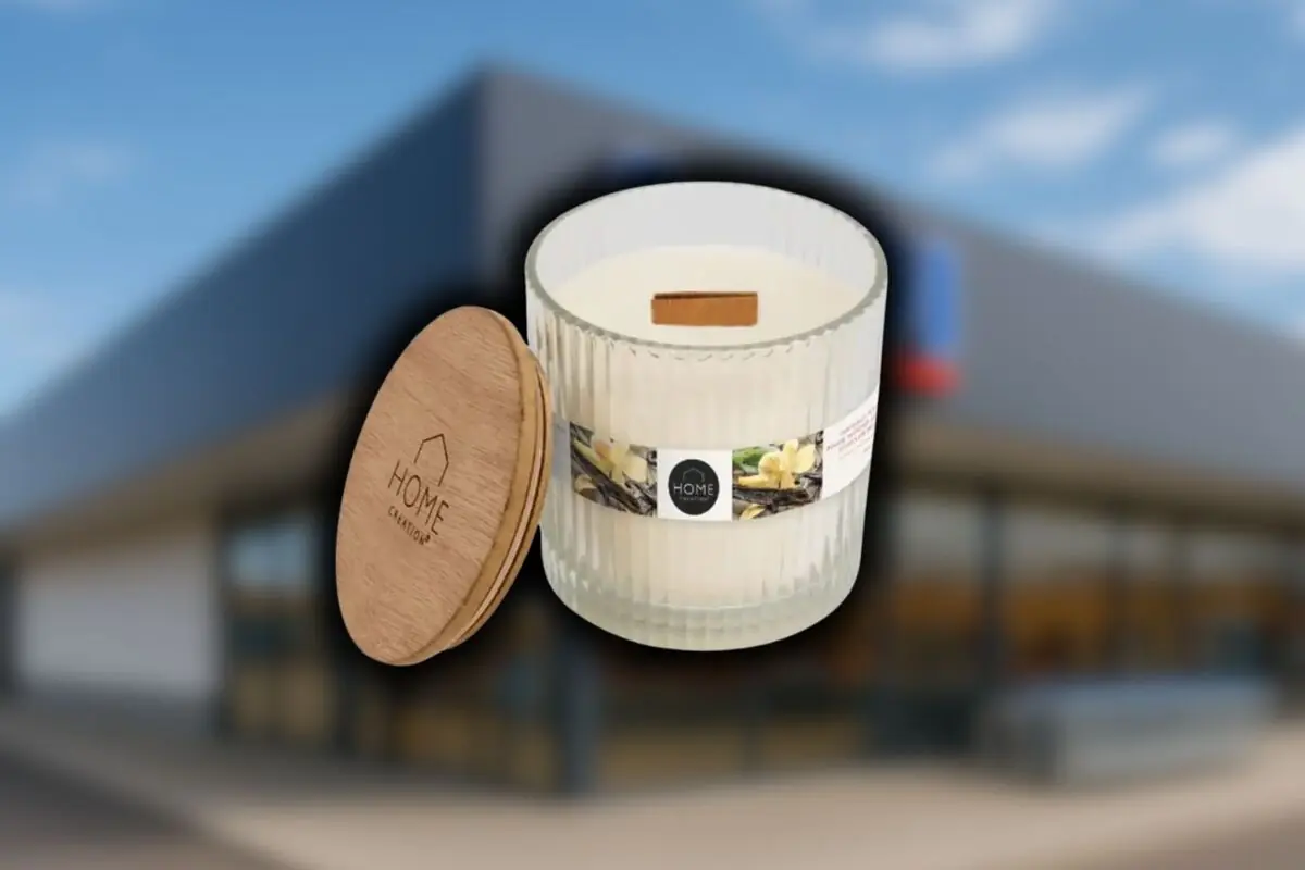 Vela aromática de vainilla en vaso de cristal con tapa de madera marca Home Creation de Aldi, frente a una tienda desenfocada.