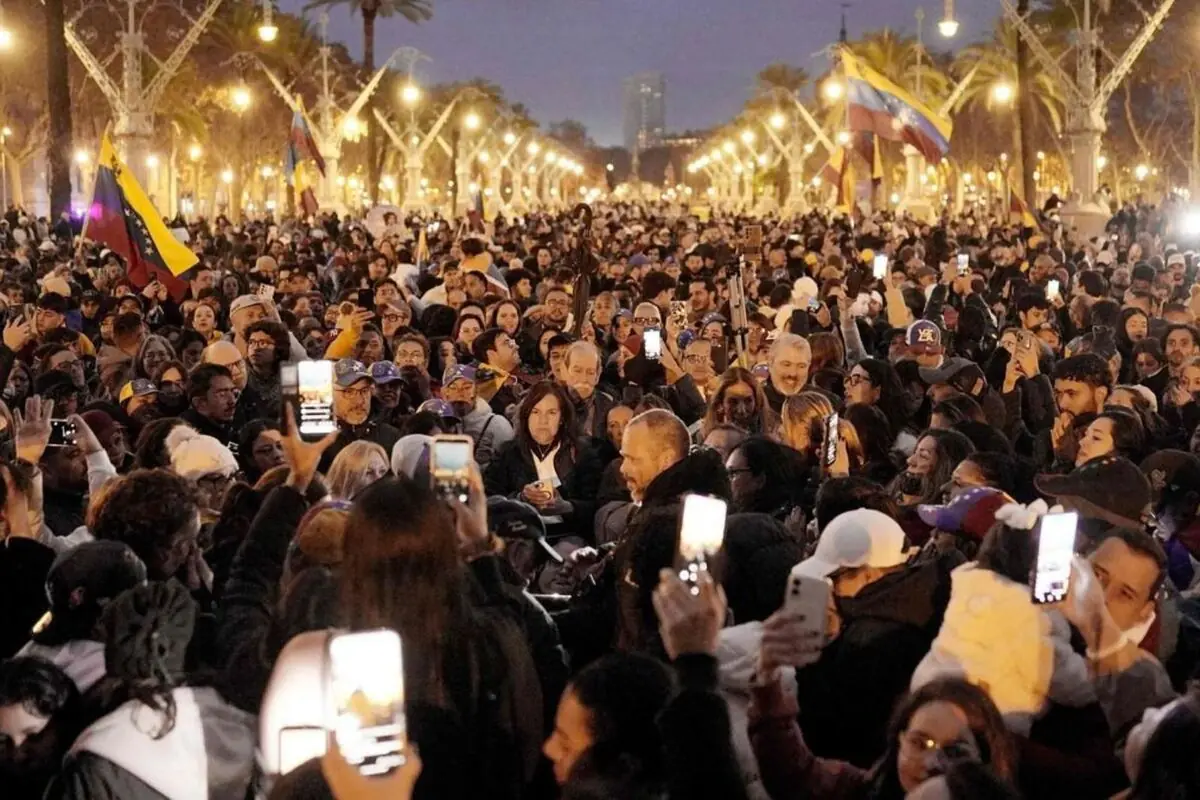 Multitud reunida de nit en una avinguda il·luminada amb moltes persones aixecant telèfons mòbils i diverses banderes de Veneçuela onejant sobre la gent