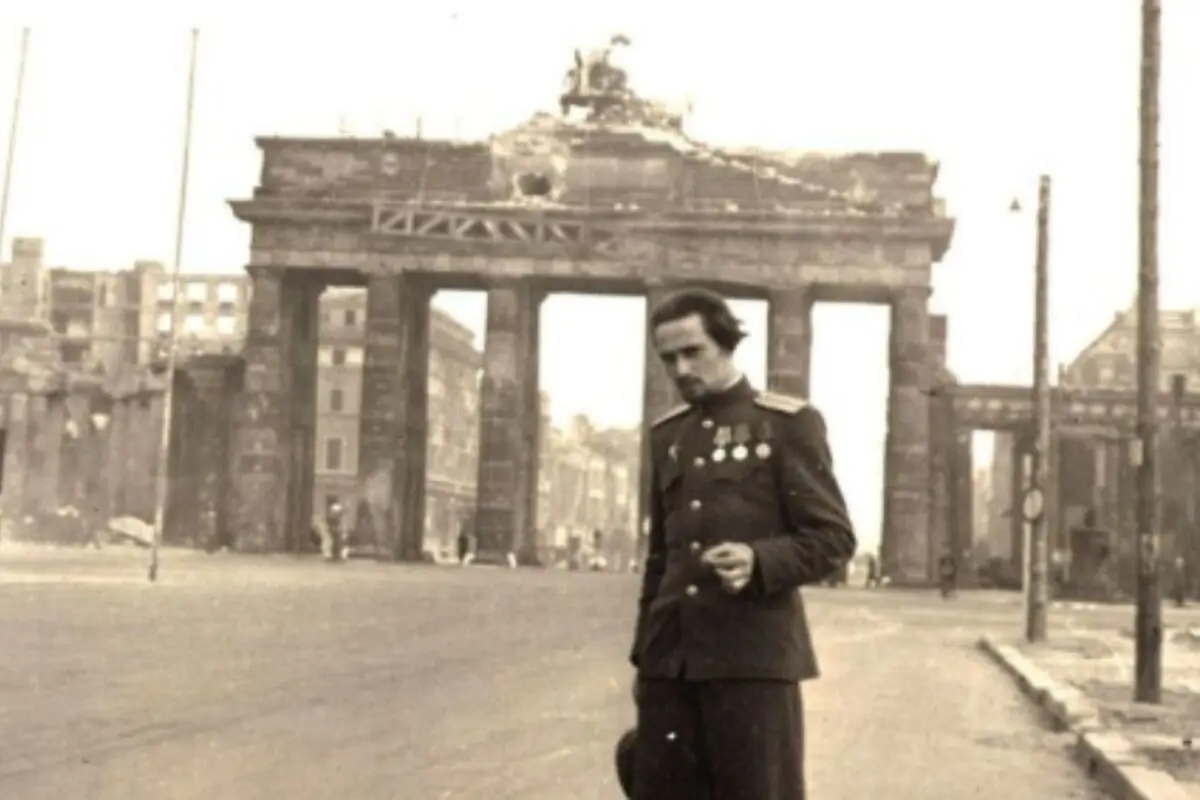 Vladímir Natánovitx Gelfand amb uniforme i medalles caminant davant la Porta de Brandenburg en una ciutat devastada després de la guerra.