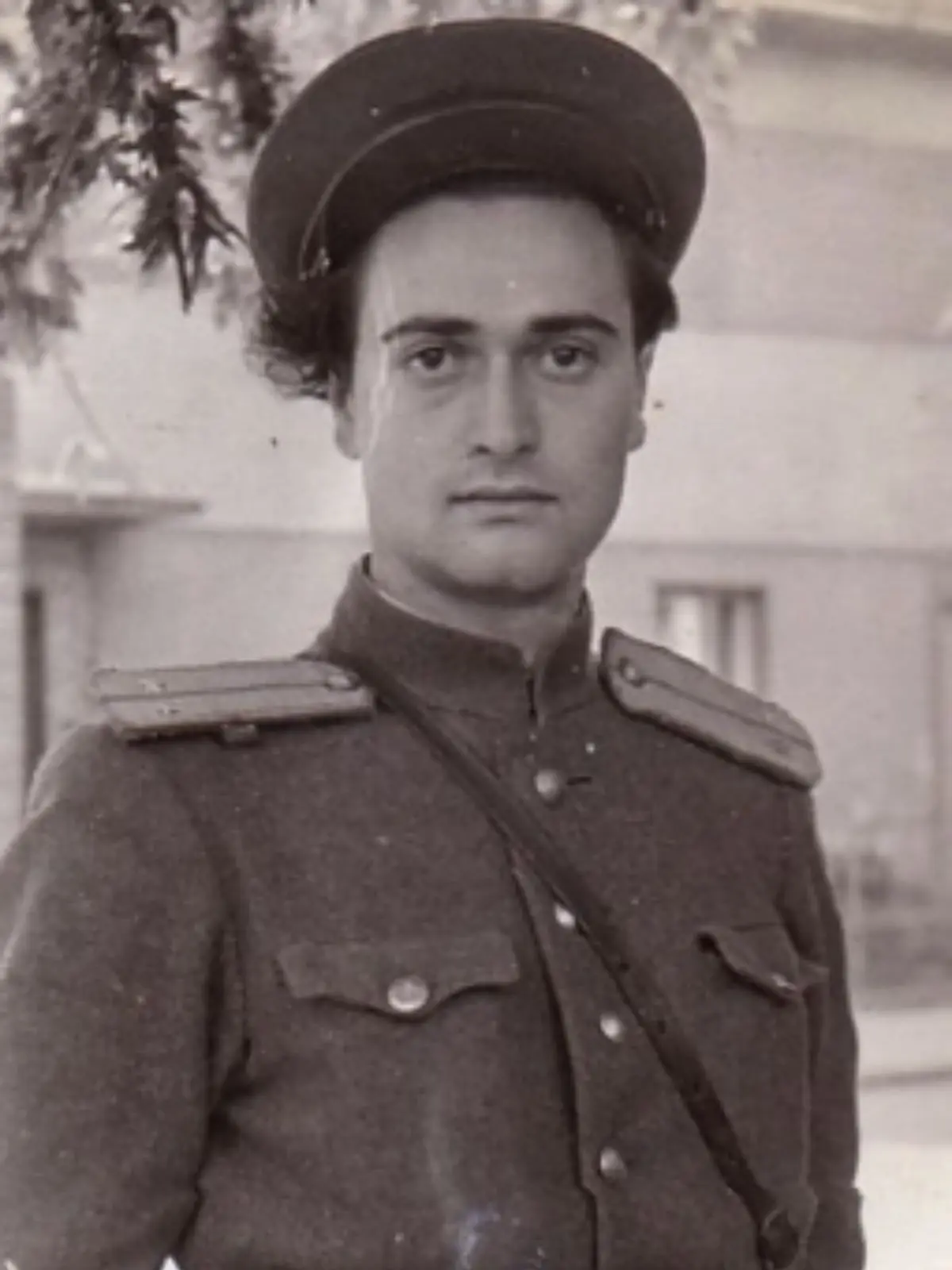 Retrat en blanc i negre de Vladímir Natànovitx Gelfand amb uniforme militar i gorra mirant a la càmera en un entorn urbà.