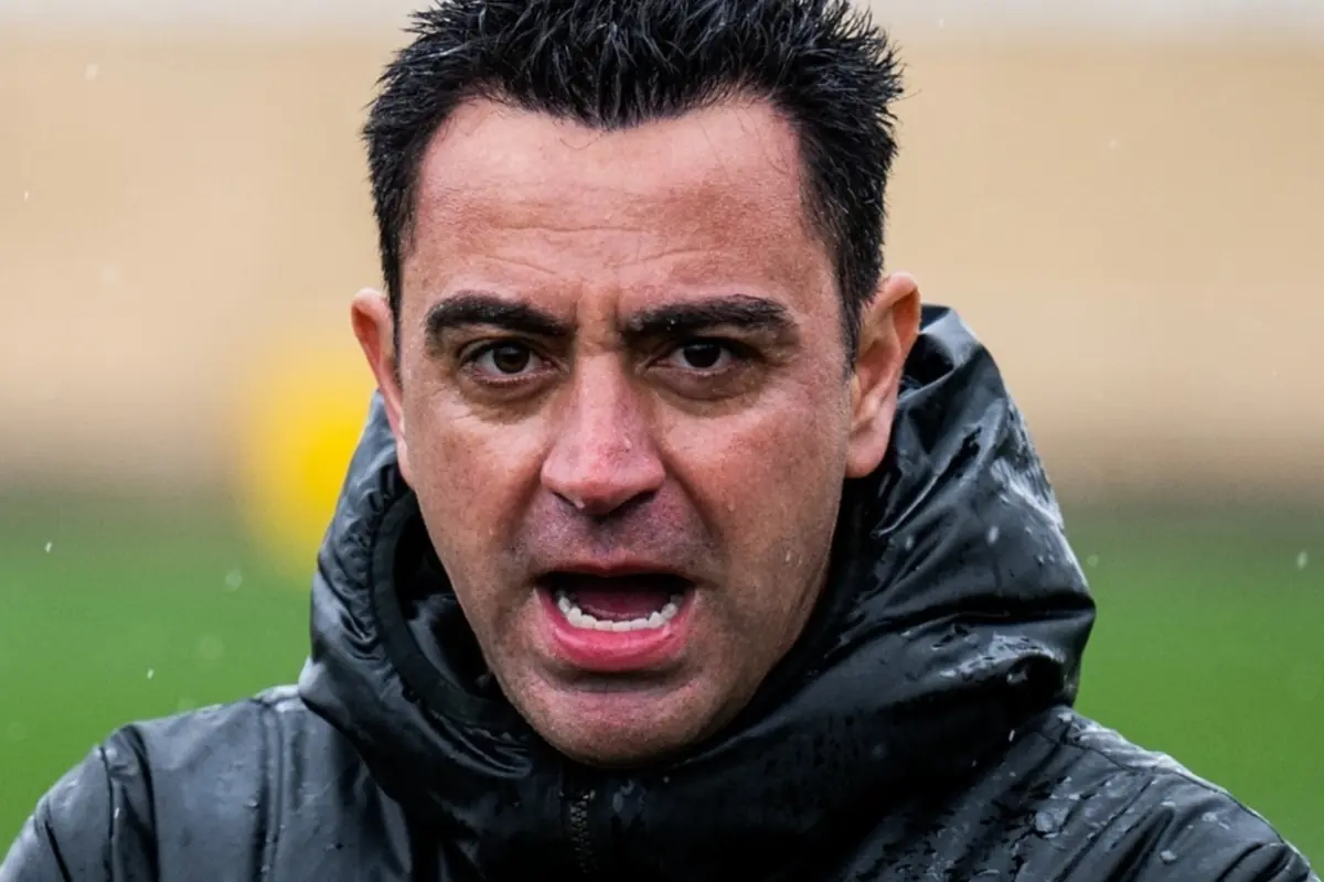 Hombre con chaqueta impermeable negra hablando bajo la lluvia en un campo de fútbol